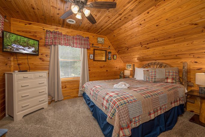 Cozy bedroom with wooden walls, a queen bed, and a TV, featuring rustic decor.