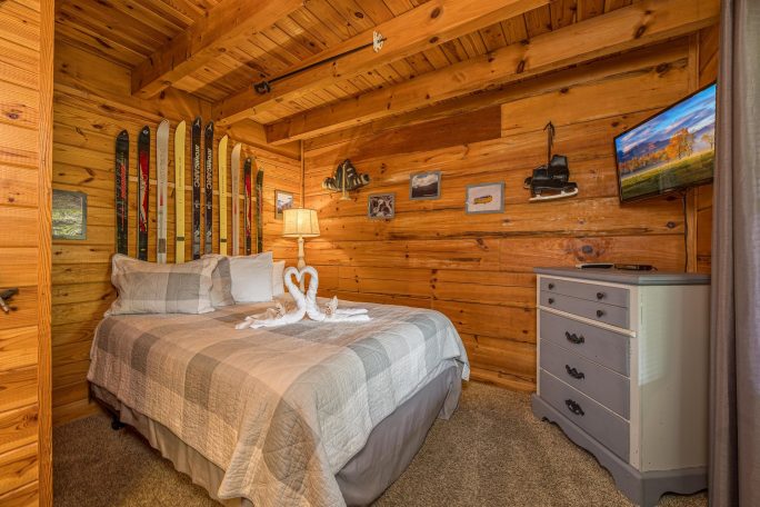 Cozy wooden bedroom with a double bed, lamp, TV, and decorative ski-themed accents.