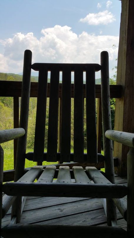 A weathered rocking chair on a porch with a view of blue skies and clouds.